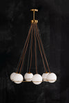 A contemporary pendant light fixture with six white milk glass globes and a minimalist brass frame, connected by thin cables.