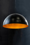 A Regan Dome Pendant light fixture with a matte black exterior and gold interior, hanging against a dark background.
