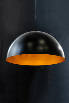 A Regan Dome Pendant light fixture with a matte black exterior and gold interior, hanging against a dark background.