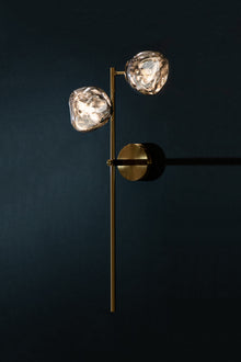  A wall sconce right facing with two globe-shaped lights, featuring a satin brass finish with black accents on the backplate, mounted on a dark wall.