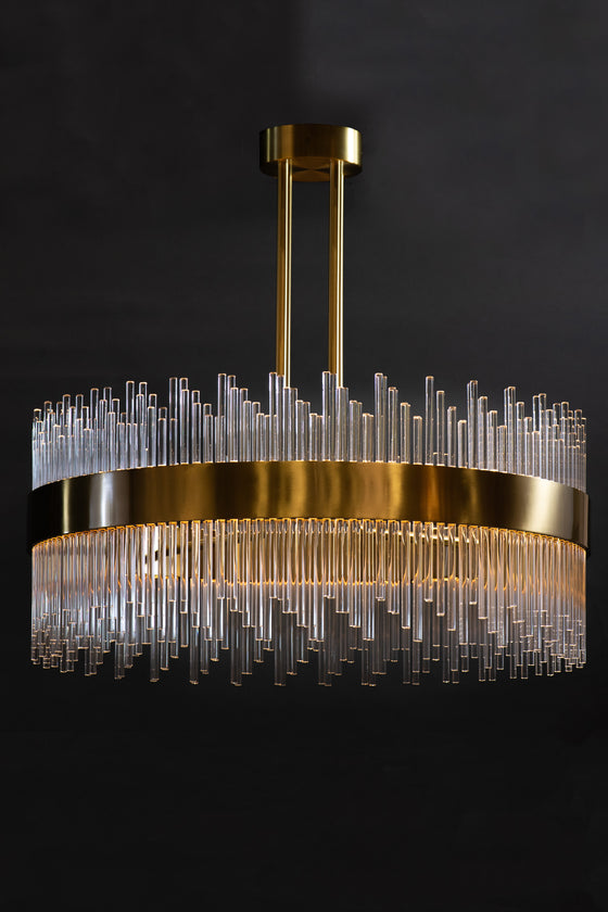 A modern satin brass chandelier with clear glass rods, hanging against a dark background.