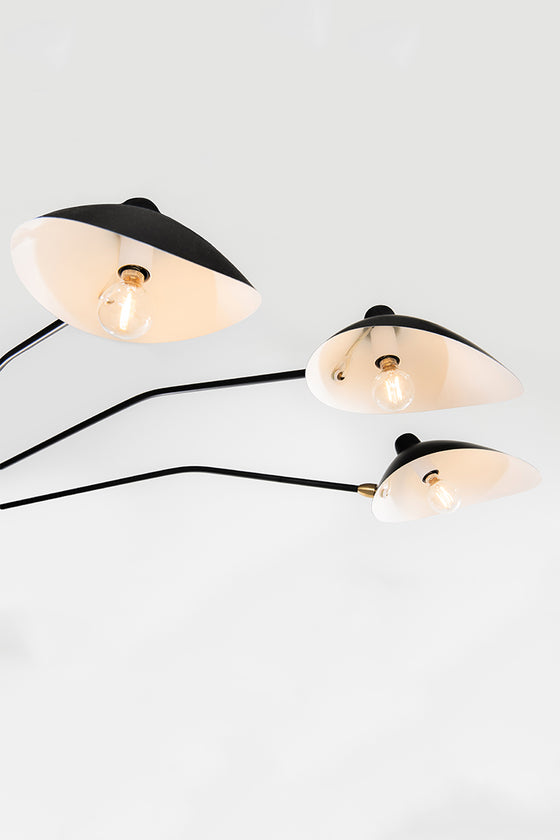 Three pendant lights with matte black shades and satin brass accents, suspended from a central point, with a white background.