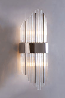  A contemporary wall sconce with staggered glass tubes and polished steel accents, illuminated for a warm glow.