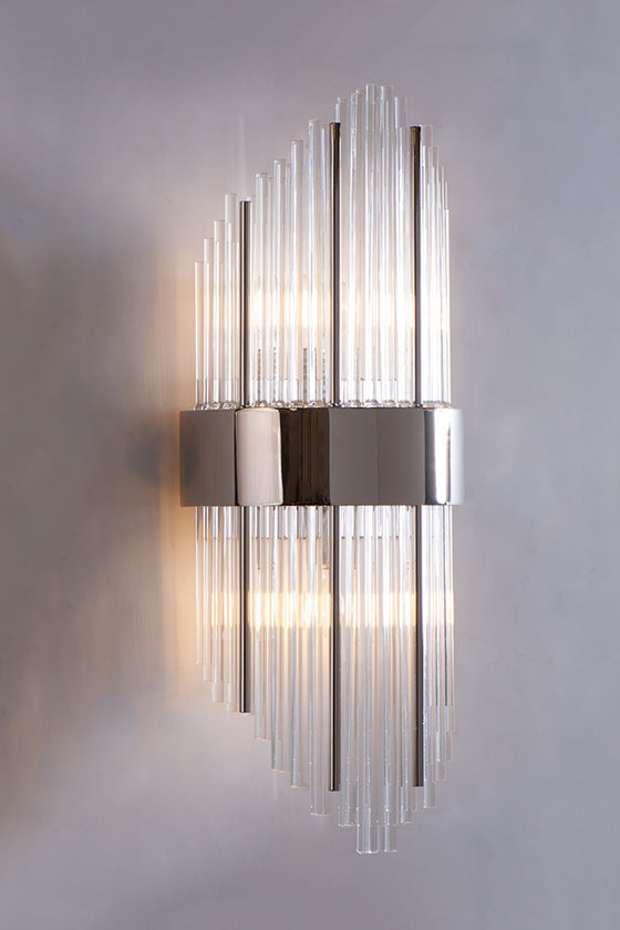 A contemporary wall sconce with staggered glass tubes and polished steel accents, illuminated for a warm glow.