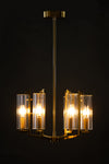 A satin brass pendant light with clear glass shades, giving off a warm glow against a dark background.