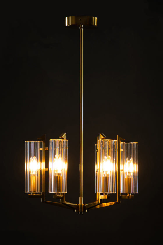 A satin brass pendant light with clear glass shades, giving off a warm glow against a dark background.