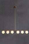 A modern linear LED chandelier with white glass globe shades, featuring a satin brass finish with matte black accent, hanging against a dark background.