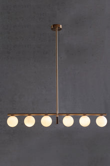  A modern linear LED chandelier with white glass globe shades, featuring a satin brass finish with matte black accent, hanging against a dark background.