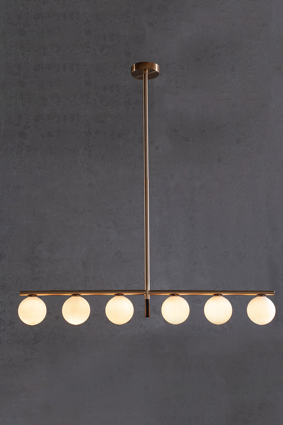 A modern linear LED chandelier with white glass globe shades, featuring a satin brass finish with matte black accent, hanging against a dark background.