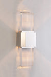 A polished nickel wall sconce with a simple geometric design featuring a beveled glass panel, emitting a bright array of light.